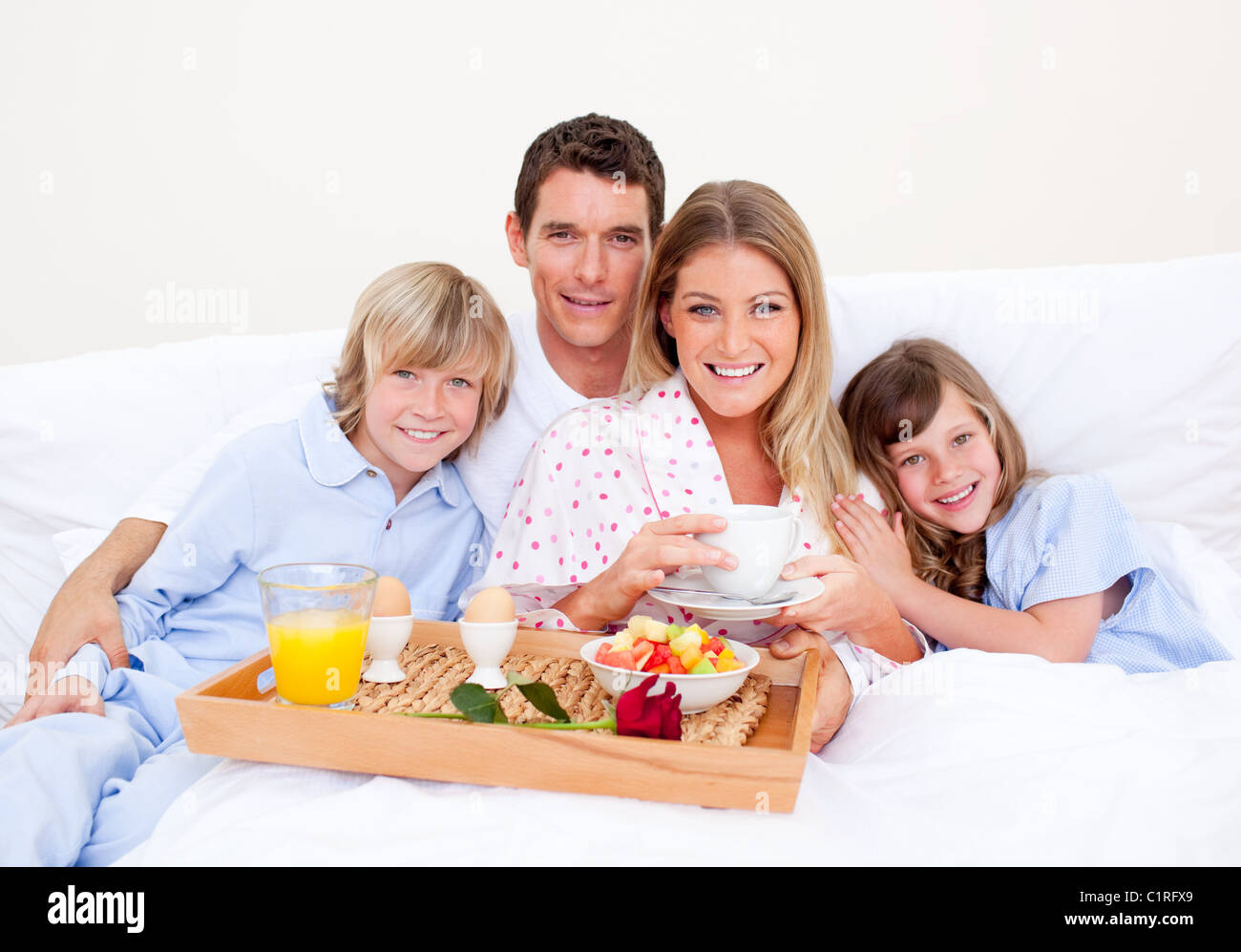 Smiling family having breakfast sitting on bed Stock Photo - Alamy