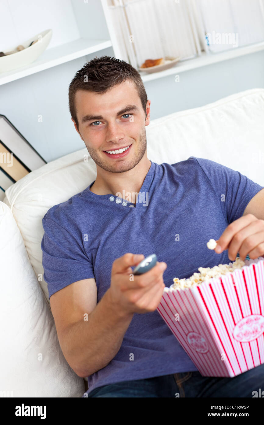 Charming young man eating popcorn watching television Stock Photo Alamy