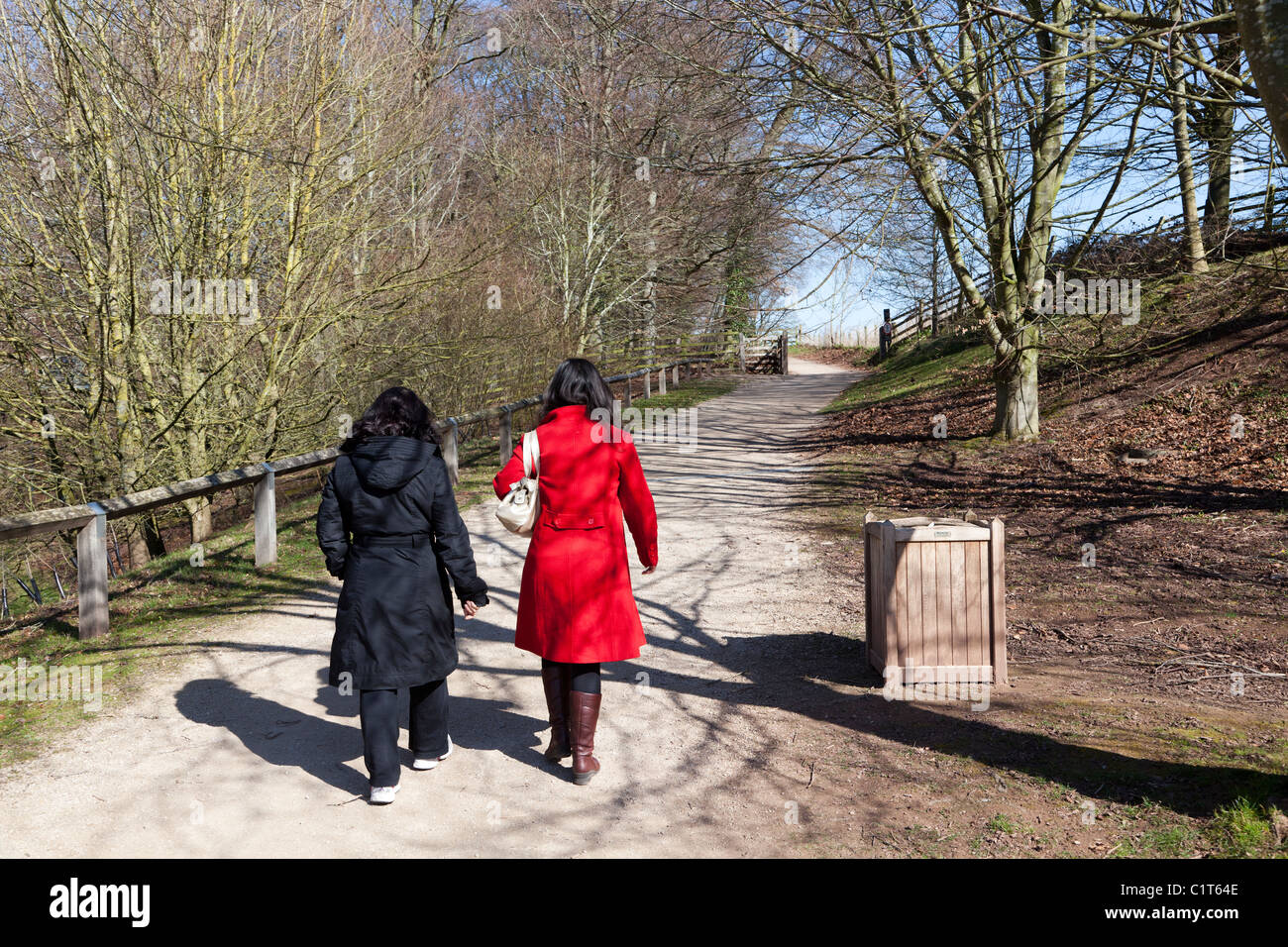 Two women in red and black clothes walking on path through woods Herefordshire England UK Stock Photo