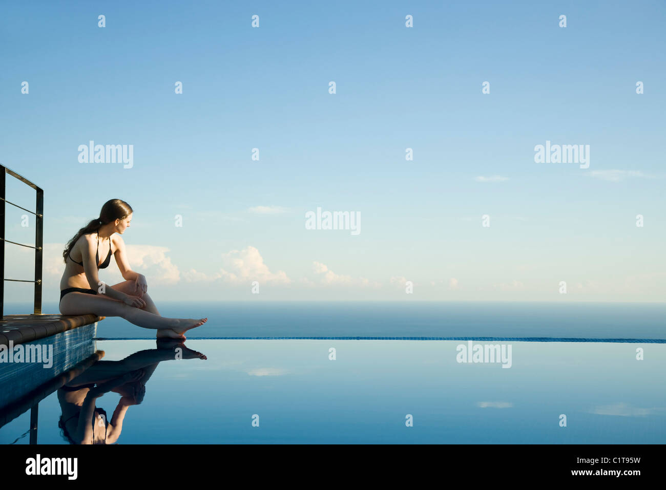 Woman sitting at edge of infinity pool, looking at view Stock Photo - Alamy