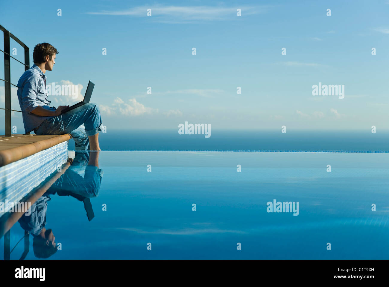 Man sitting at edge of infinity pool with laptop computer, looking at ...