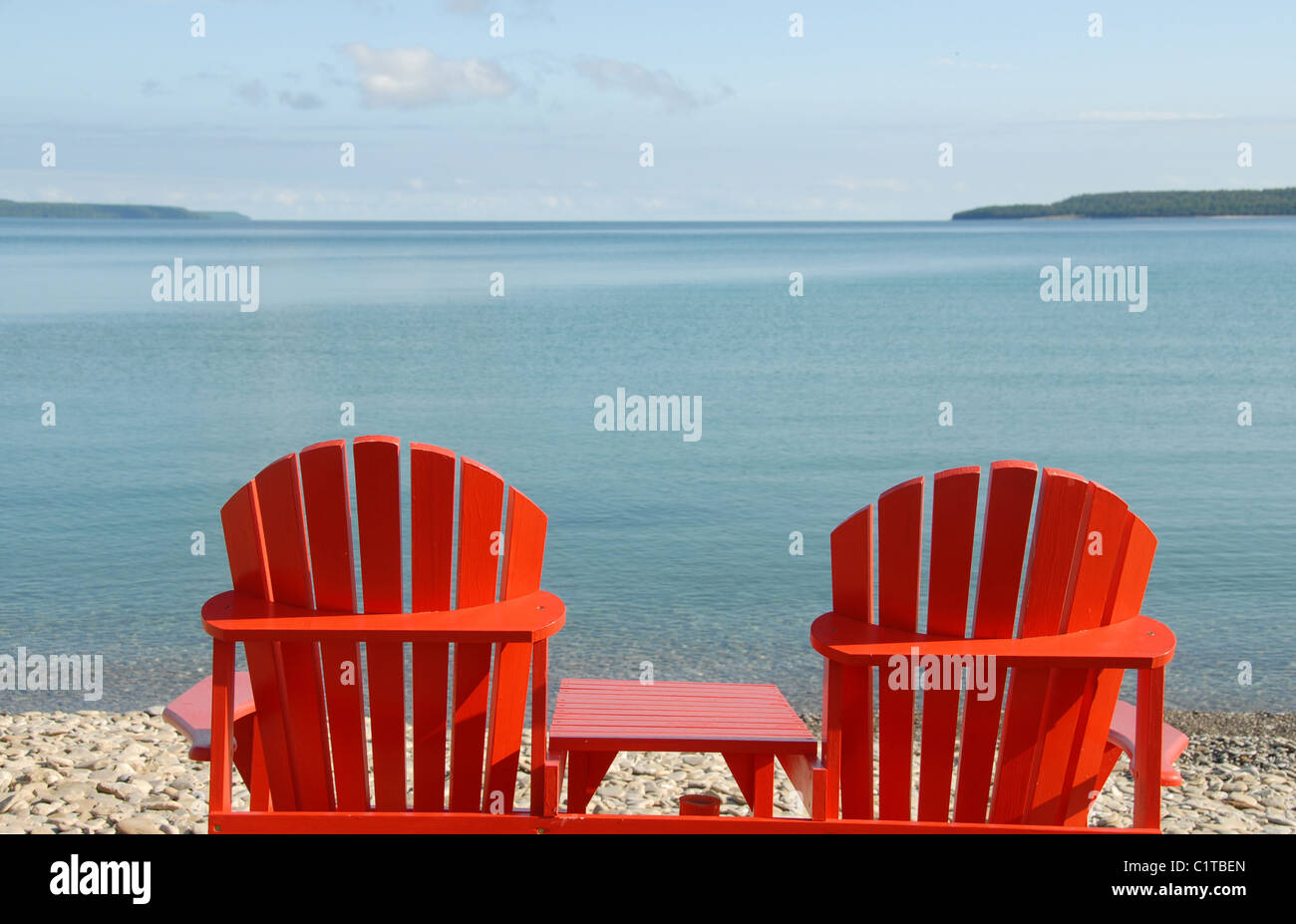 Summer in Canada: Two red Muskoka chairs on the pebble beach of Big Bay facing the Owen Sound of Georgian Bay in Ontario Stock Photo