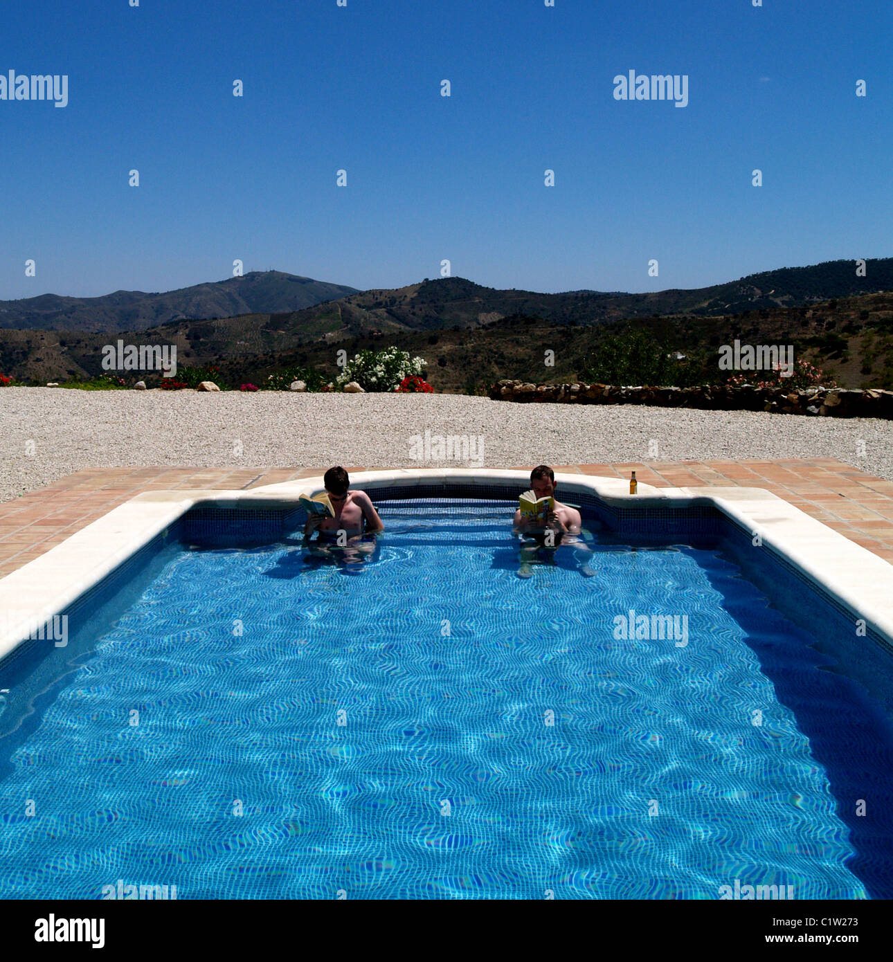 Two late teenage men relax reading in a Spanish Swimming pool Stock Photo