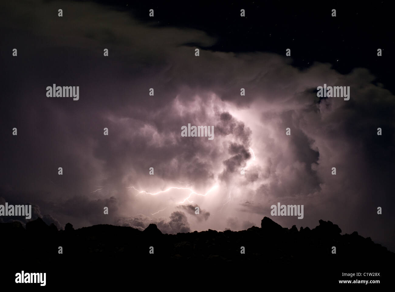 A lightning over the crater rim in the night. Below there are dense ...