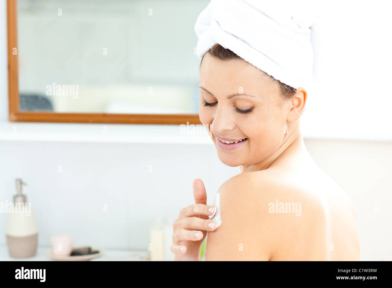 Attractive young woman with a towel putting cream on her face in the