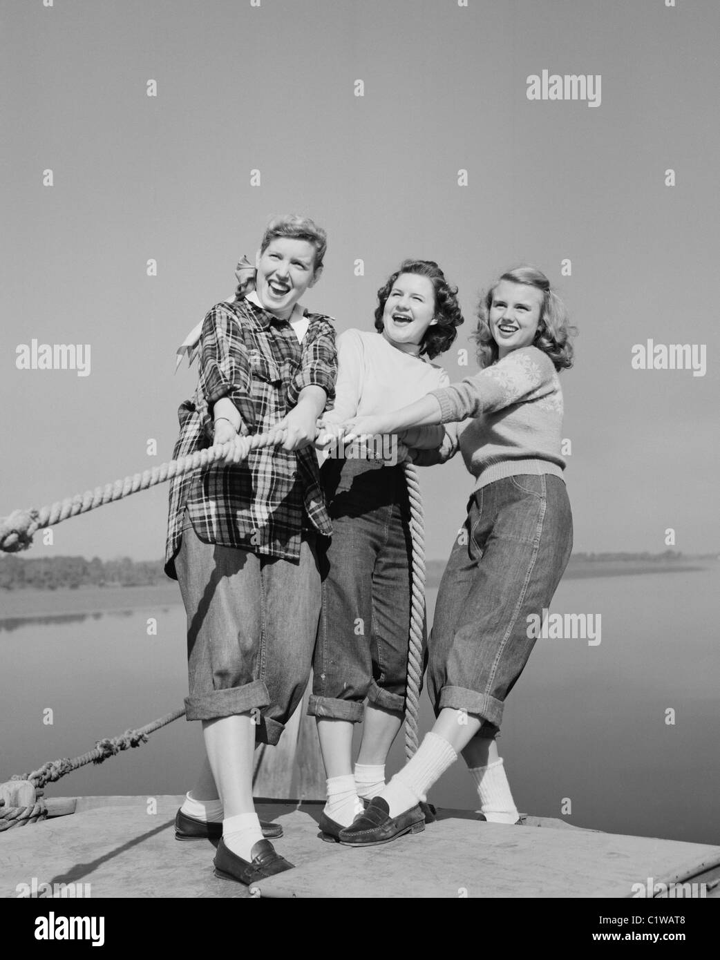 Three girls pulling rope on jetty Stock Photo