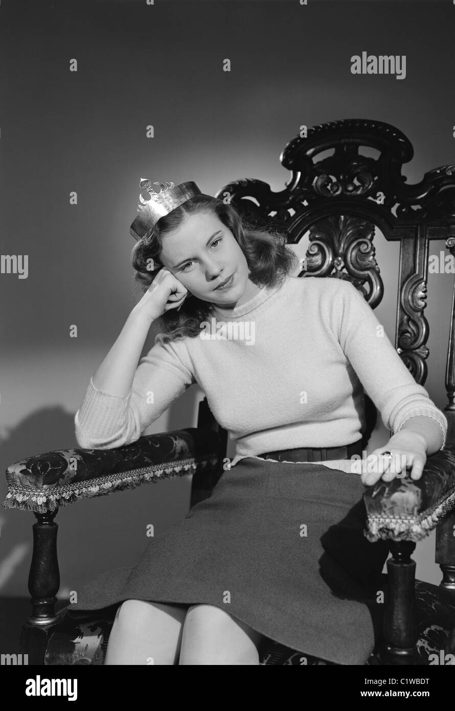 Studio shot of young woman wearing crown sitting in chair Stock Photo