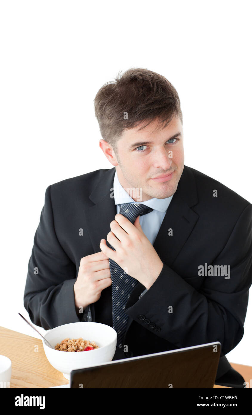 Elegant businessman having breakfast and touching his tie in front of his laptop Stock Photo
