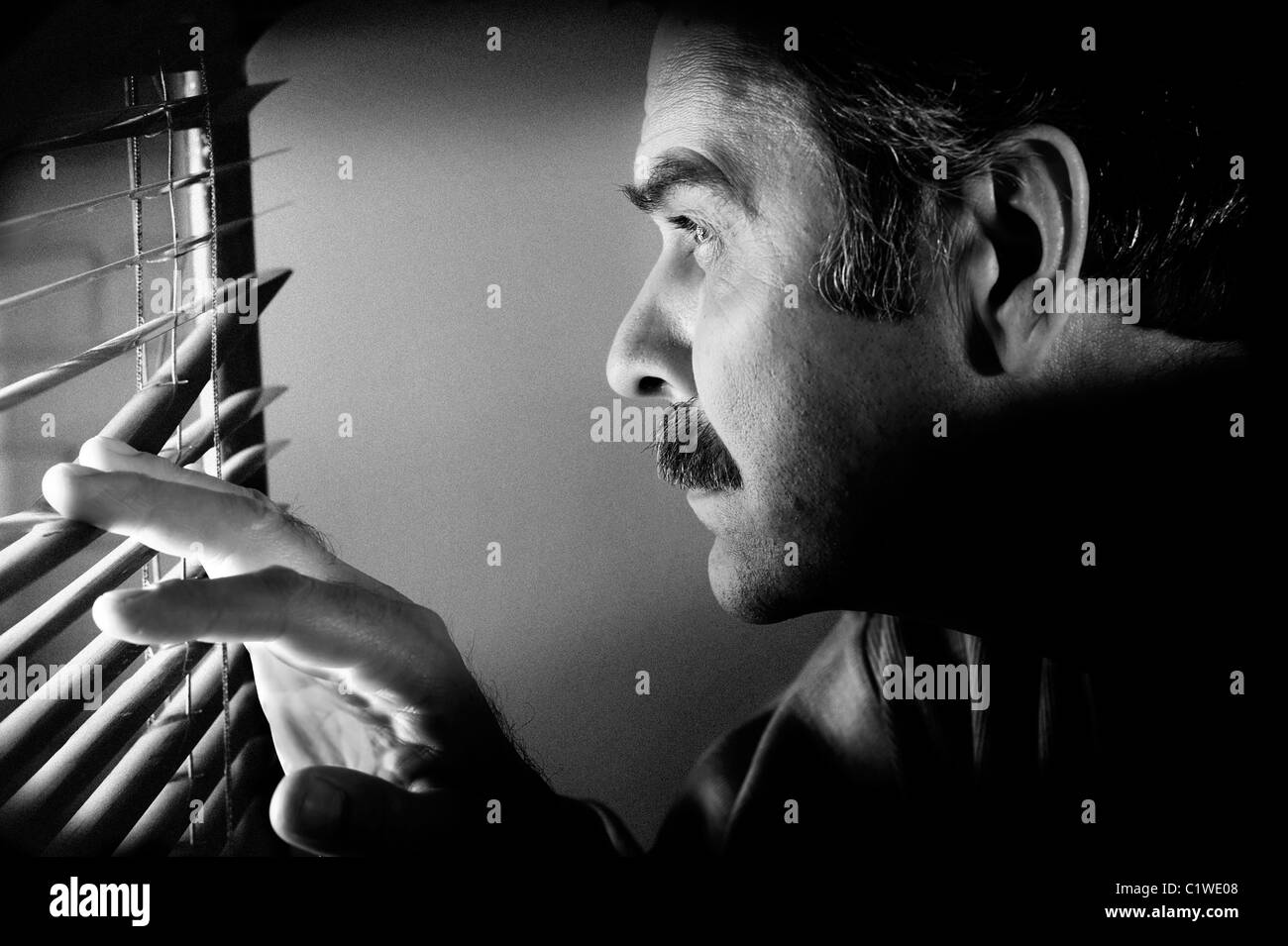 Low key concept photo of man looking furtively through window jalousie. Black&white processed image with special grained texture Stock Photo