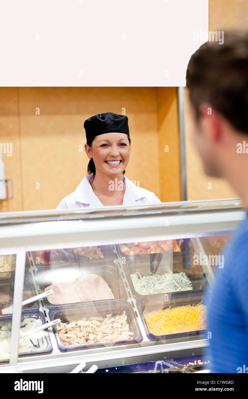 Joyful baker behind her display and customer in the queue talking