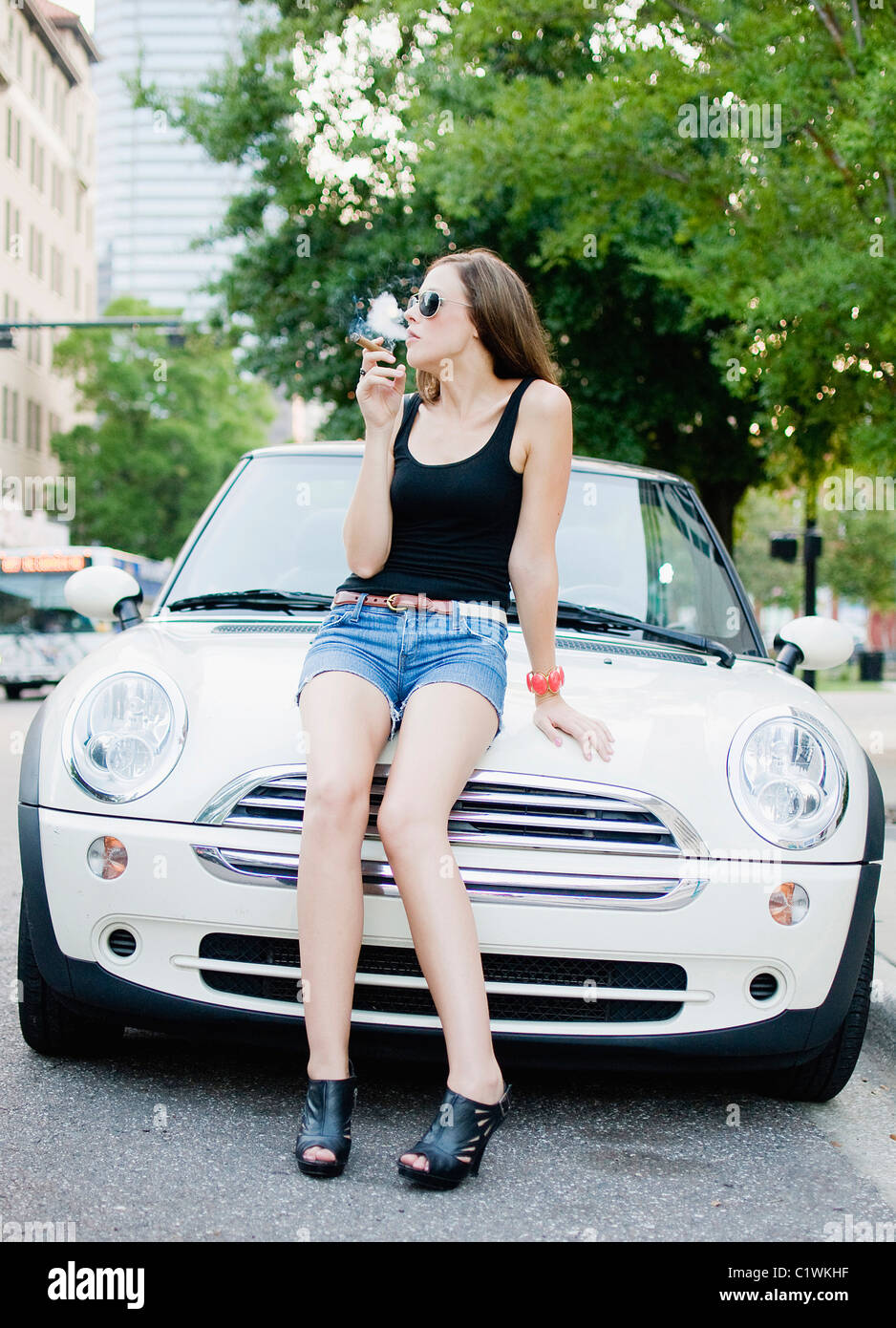 Woman sitting on the car hood and smoking a cigar Stock Photo