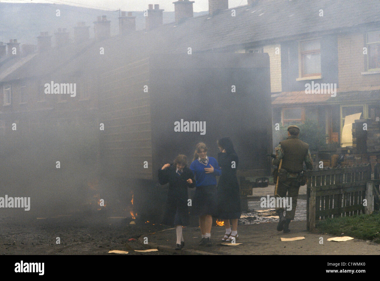 Belfast The Troubles 1980s. Three schoolgirls after school going home in school uniform walking past a burning hijacked lorry,  smoke billowing out used as a barricade. British armed soldier going to investigate whats going on.  Northern Ireland 1981 UK HOMER SYKES Stock Photo