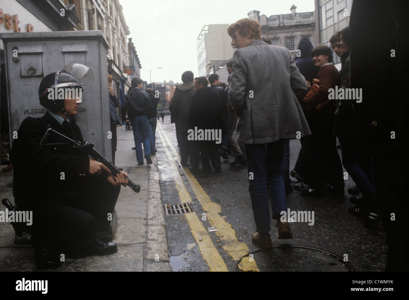 Northern Ireland The Troubles 1980s. RUC policeman on  foot patrol rifle that shoots rubber bullets centre of Belfast 1981. Group of lads   milling around potential trouble.  HOMER SYKES Stock Photo