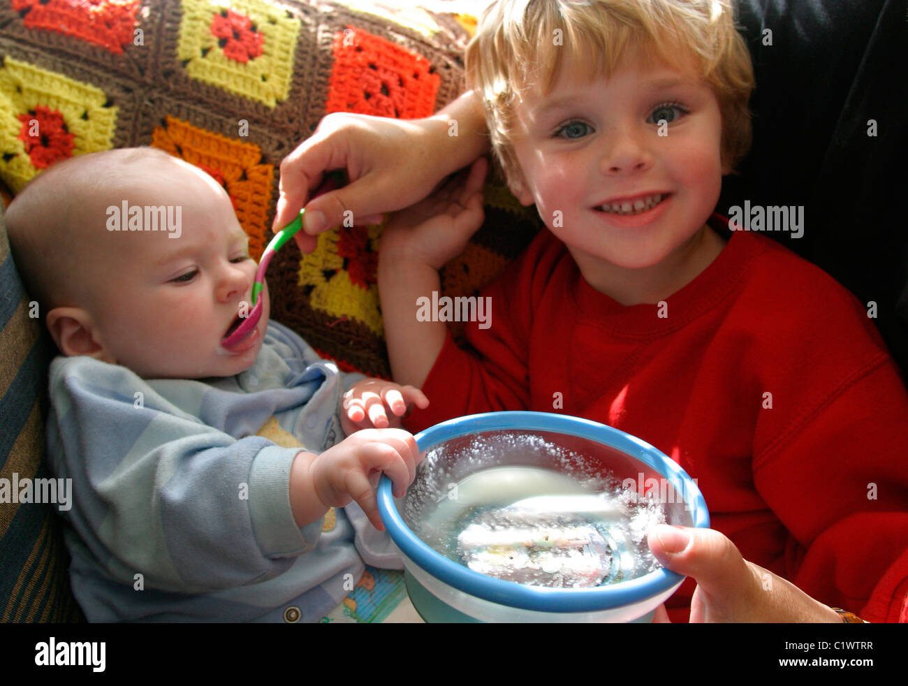 A helpful 5 Year old boy feeding lunch to his baby brother Stock Photo