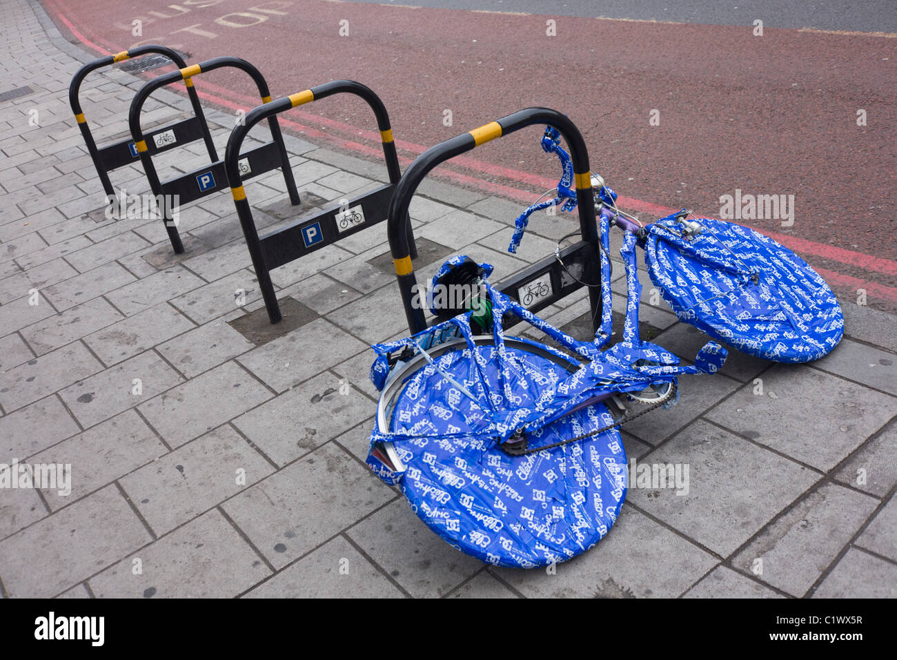 A ladies bike covered in blue plastic wrapping tape is locked up