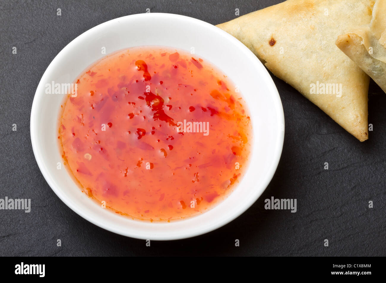 Sweet chilli dipping sauce and golden fried samosa's on dark slate background. Stock Photo