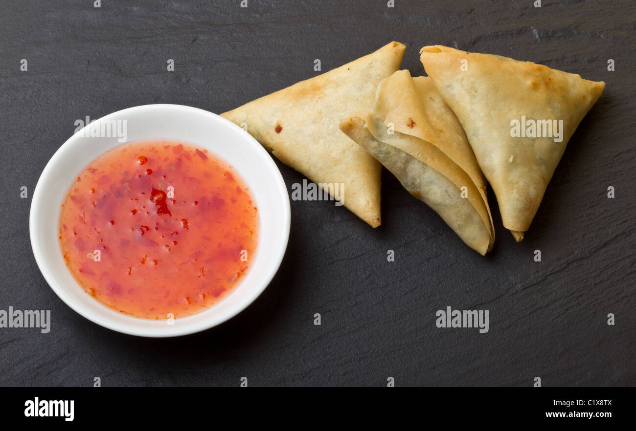 Sweet chilli dipping sauce and golden fried samosa's on dark slate background. Stock Photo