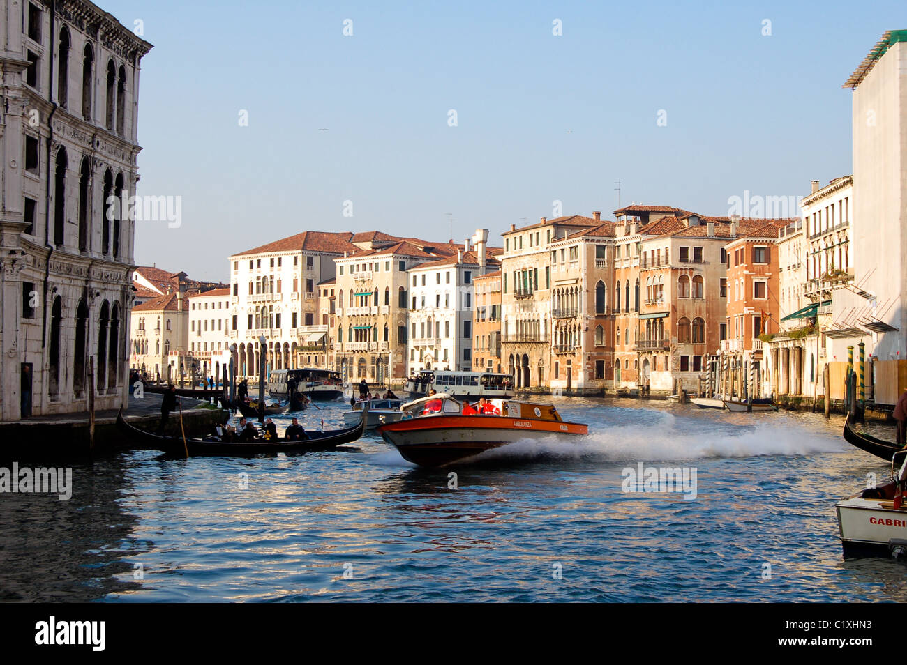 Water ambulance speeds down a canal, in warm near sunset light, Venice, Italy Stock Photo