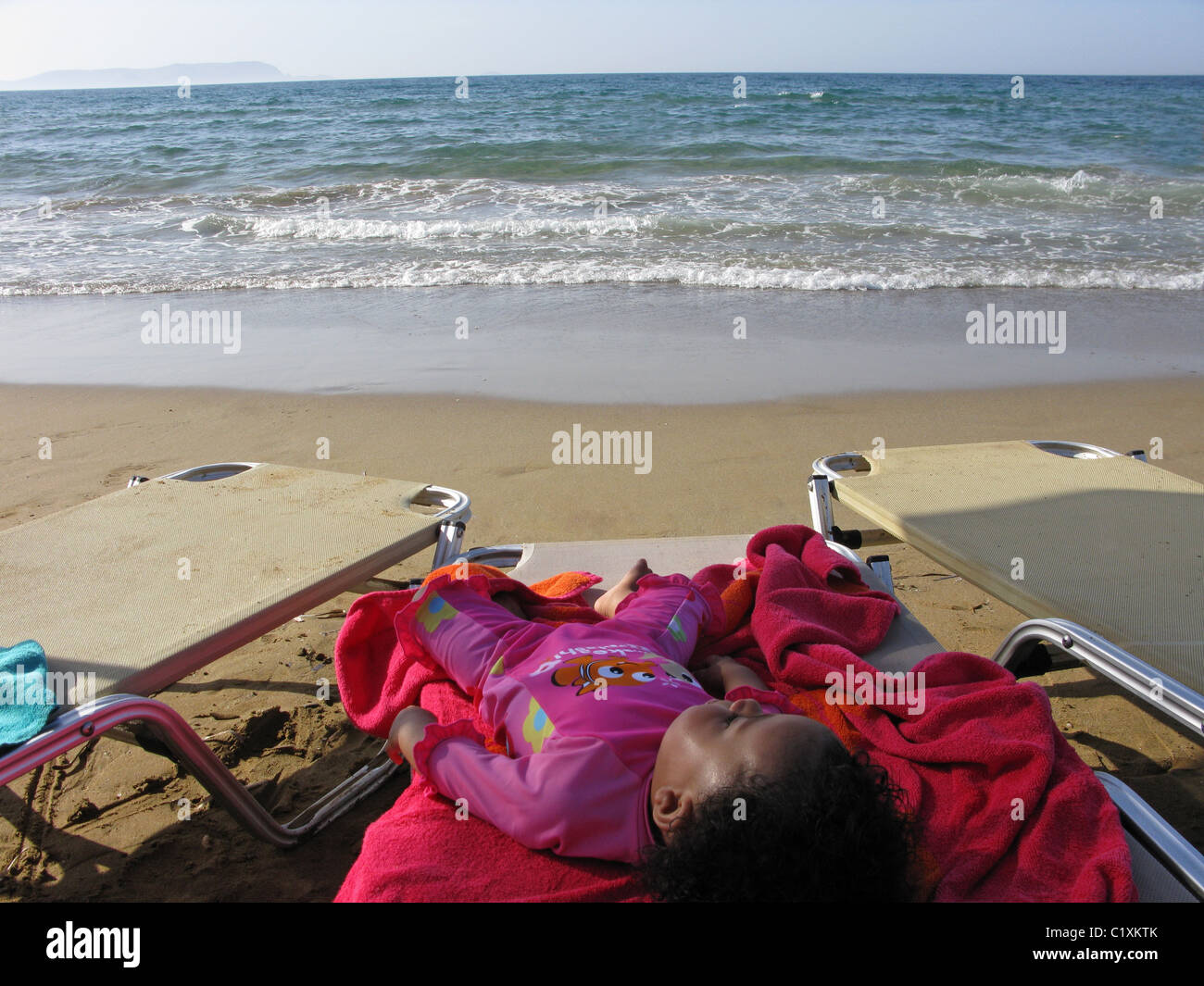 Baby wearing a sun protection swim suit, sleeps under a parasol on a
