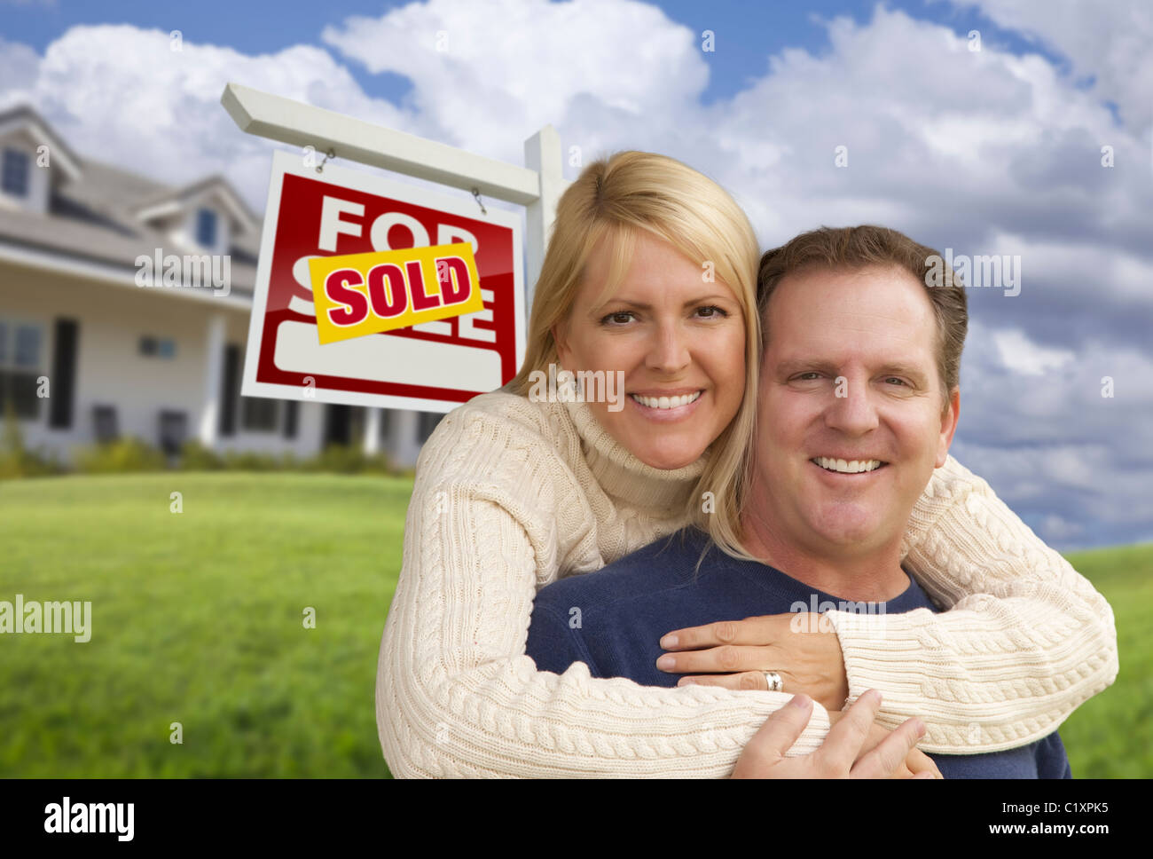 Happy Couple Hugging in Front Yard with Sold Real Estate Sign and House ...