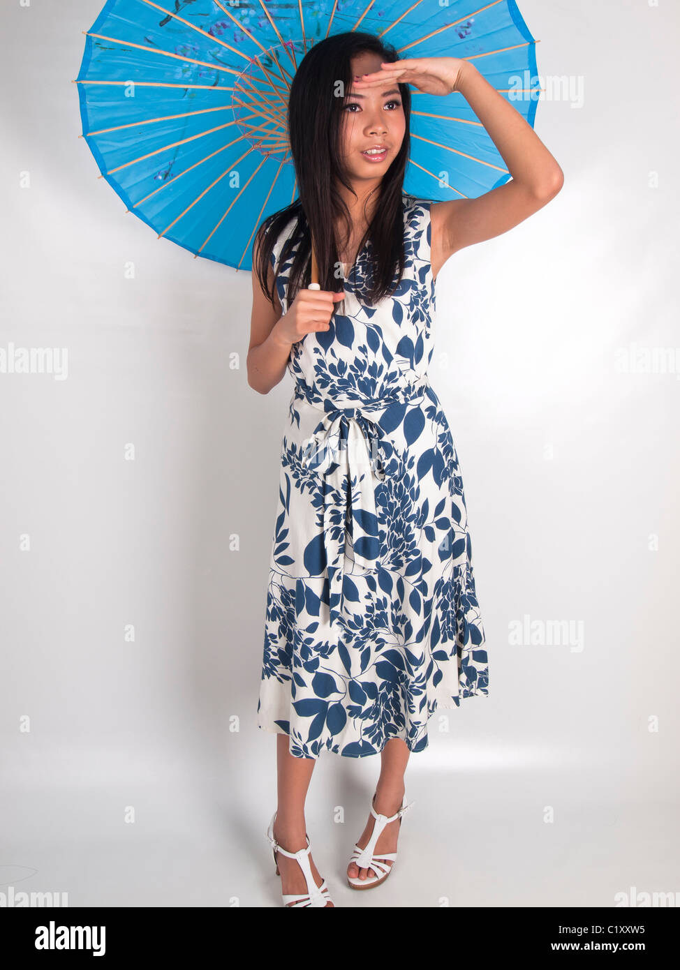 A young girl under a blue umbrella looking out for something Stock Photo