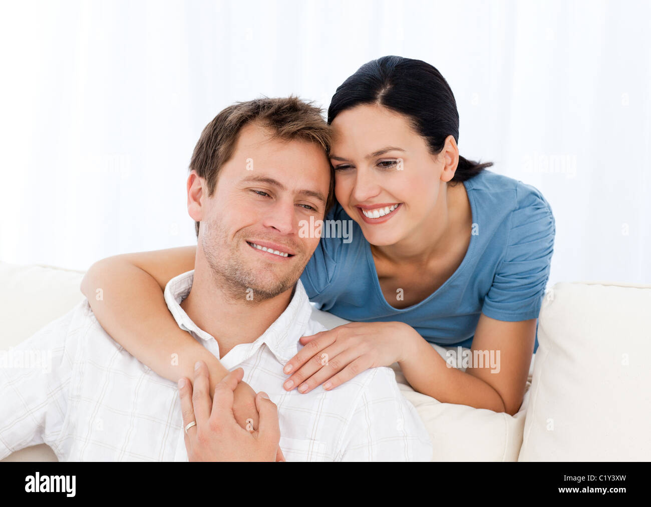 Lovely woman hugging her boyfriend while relaxing on the sofa Stock Photo