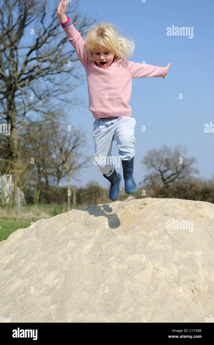 Stock photo of a five year old girl jumping off a pile of sand. Stock Photo