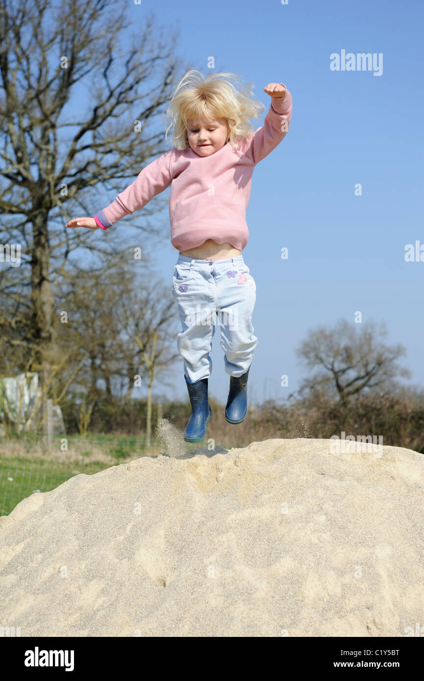 Stock photo of a five year old girl jumping off a pile of sand. Stock Photo