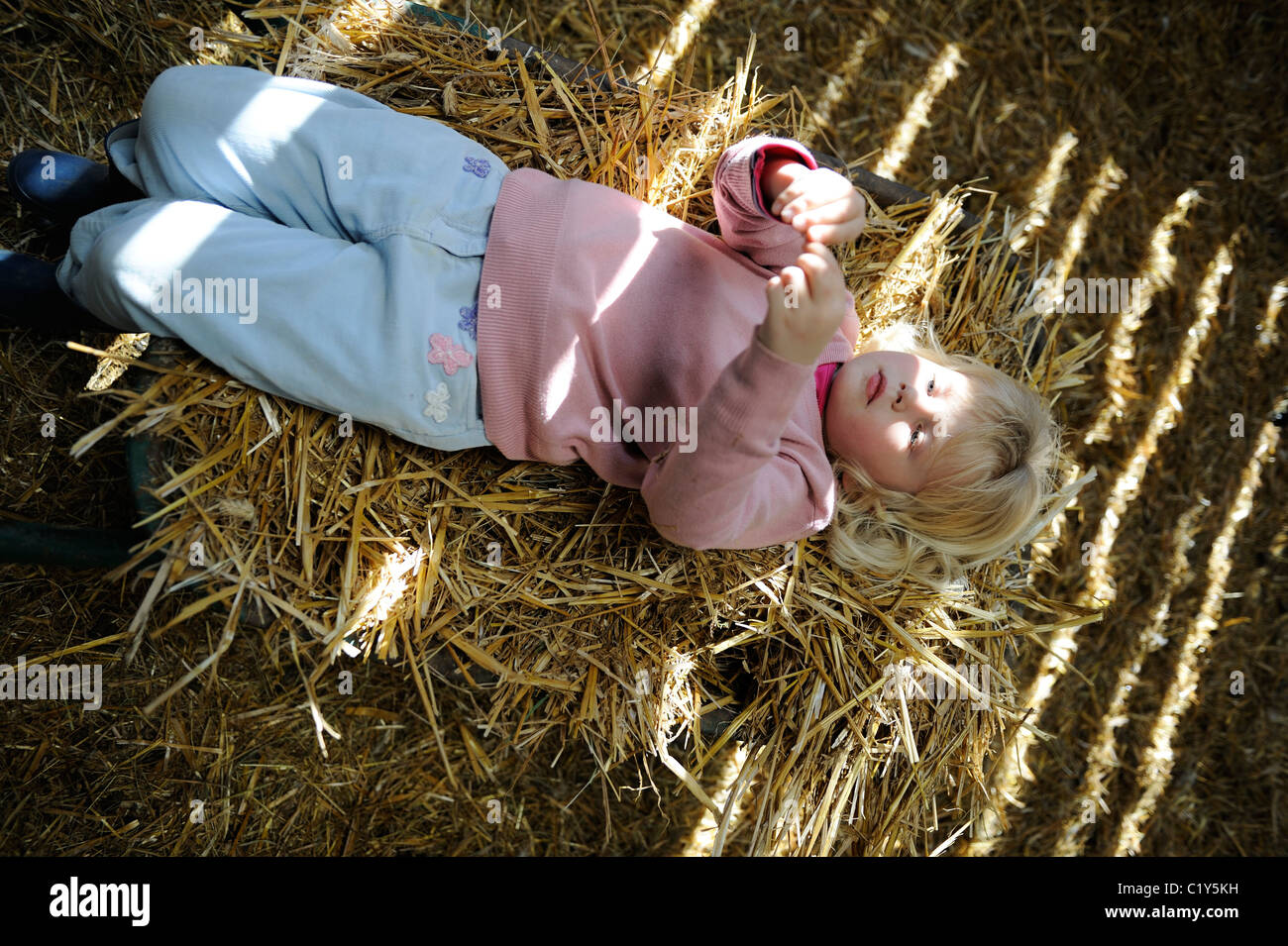 Stock photo of a five year old girl lying on a wheelbarrow filled with straw. Stock Photo