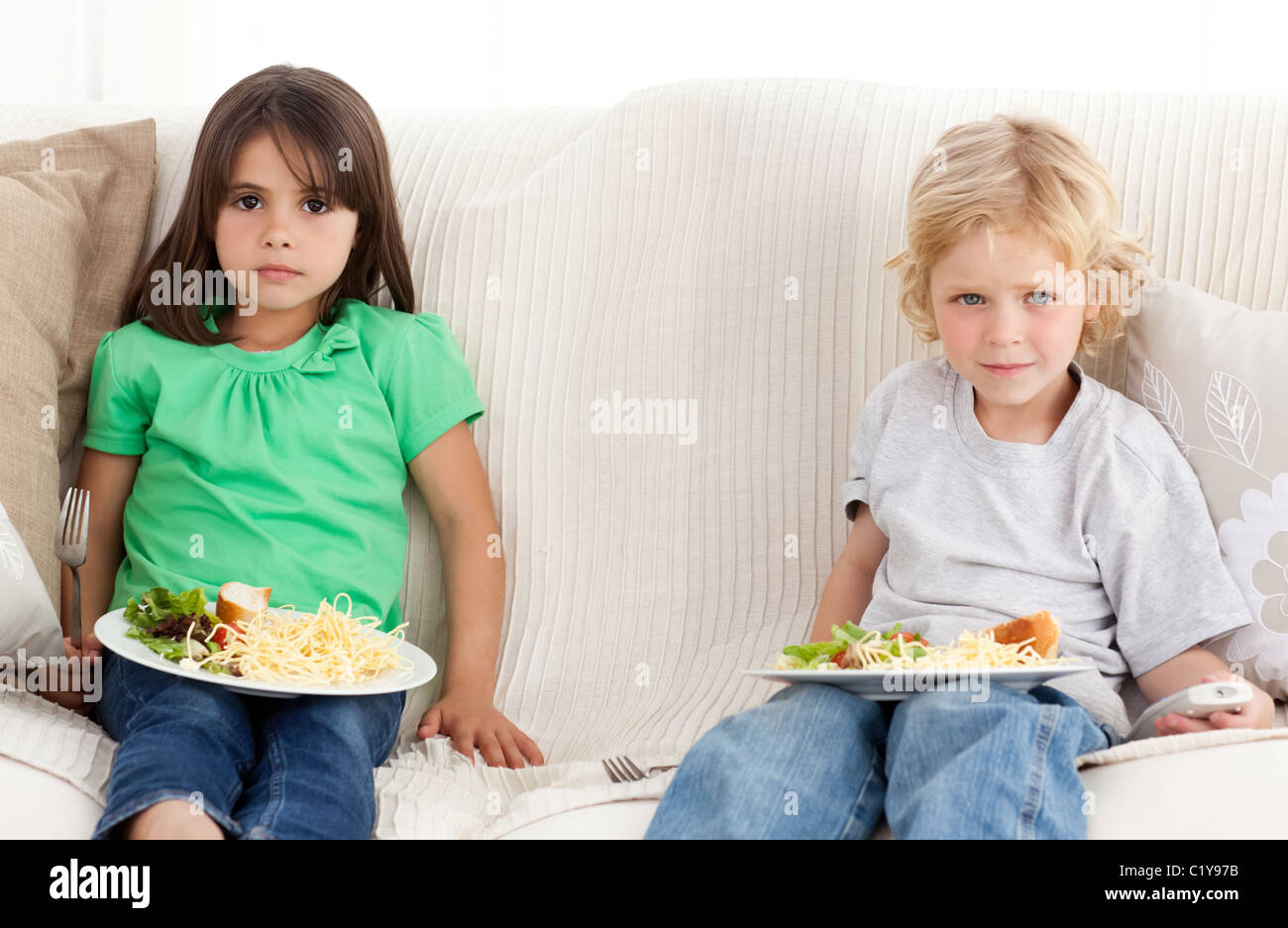 Serious brother and sister having dinner on the sofa Stock Photo Alamy
