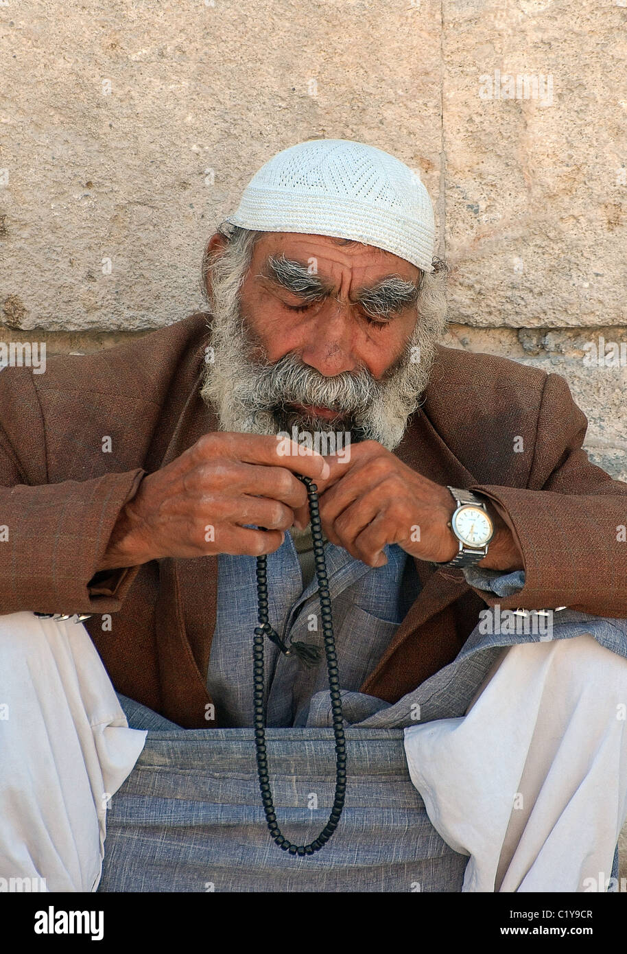 An elderly Syrian man with a gray beard thoughtfully sits and prays his prayer beads, Aleppo, Syria Stock Photo
