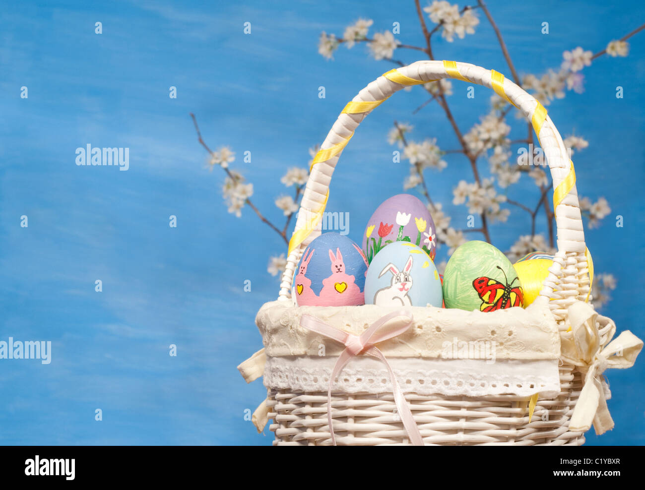 Colorful Easter basket filled with hand painted eggs, with spring twigs on blue background Stock Photo