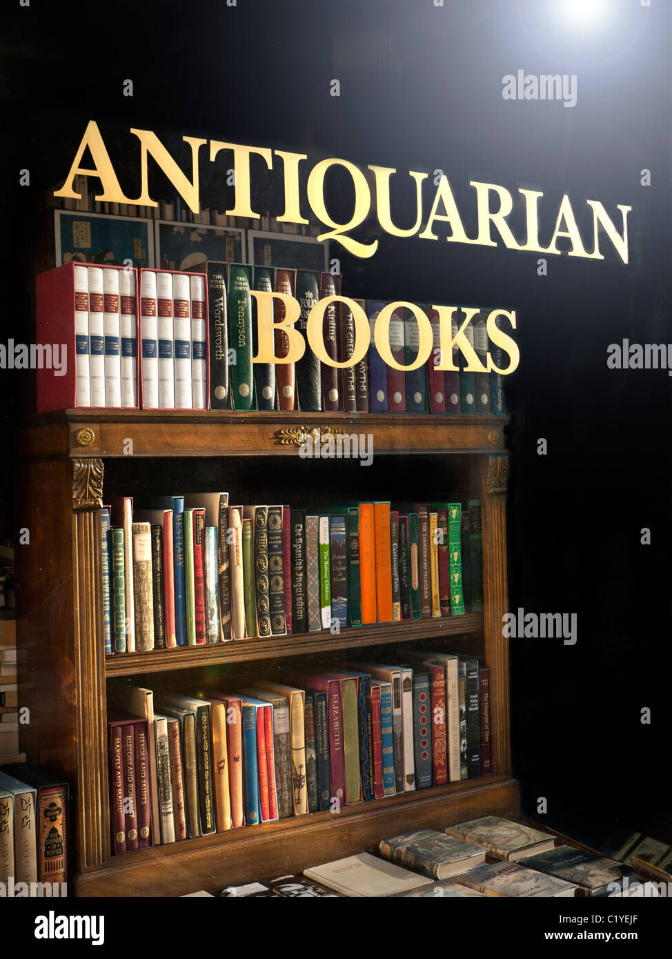 Antiquarian Bookshop window with sign and antique old books and bookcase on display with sun flaring on window glass Stock Photo