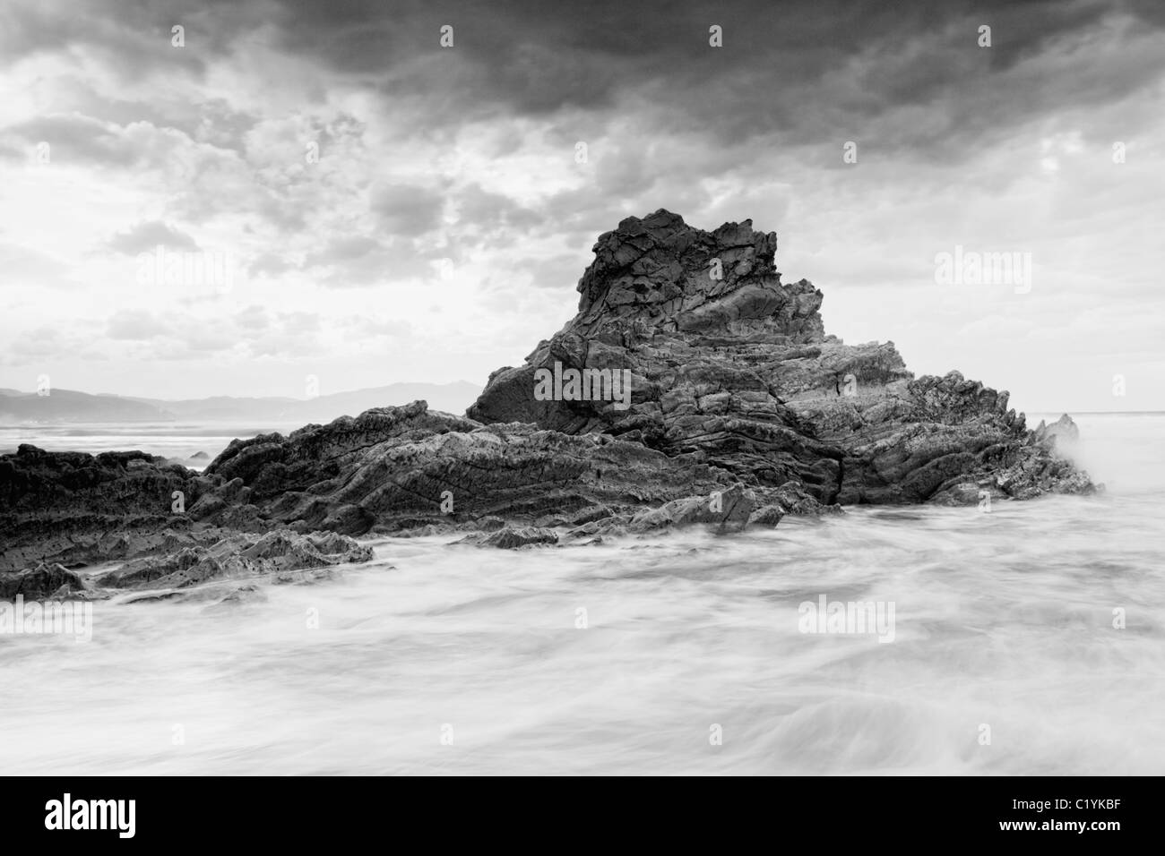 B&W seascape showing a rock on the coast with a cloudy stormy sky Stock Photo