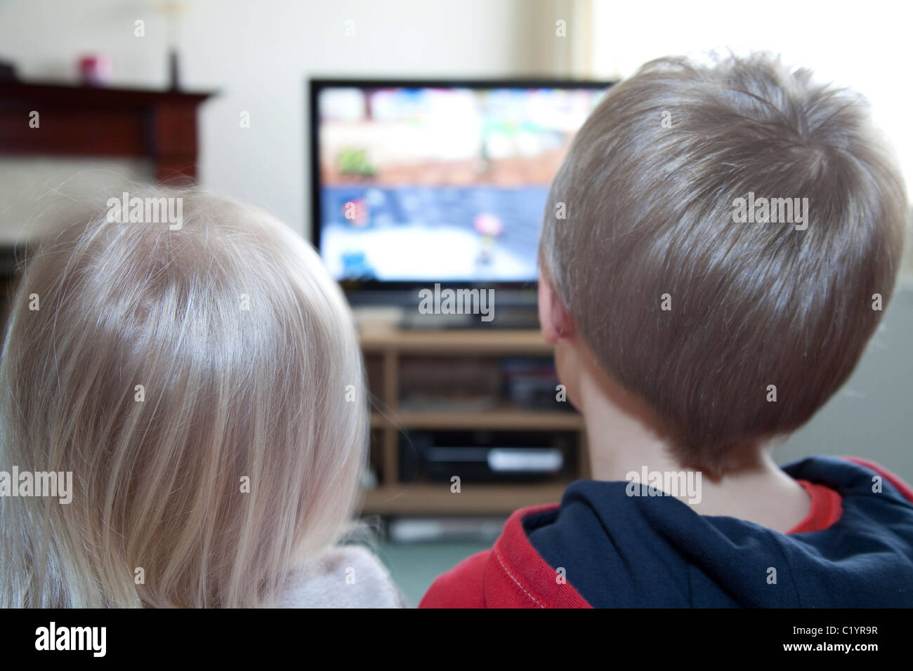 A young brother and sister watch TV together in the family home England