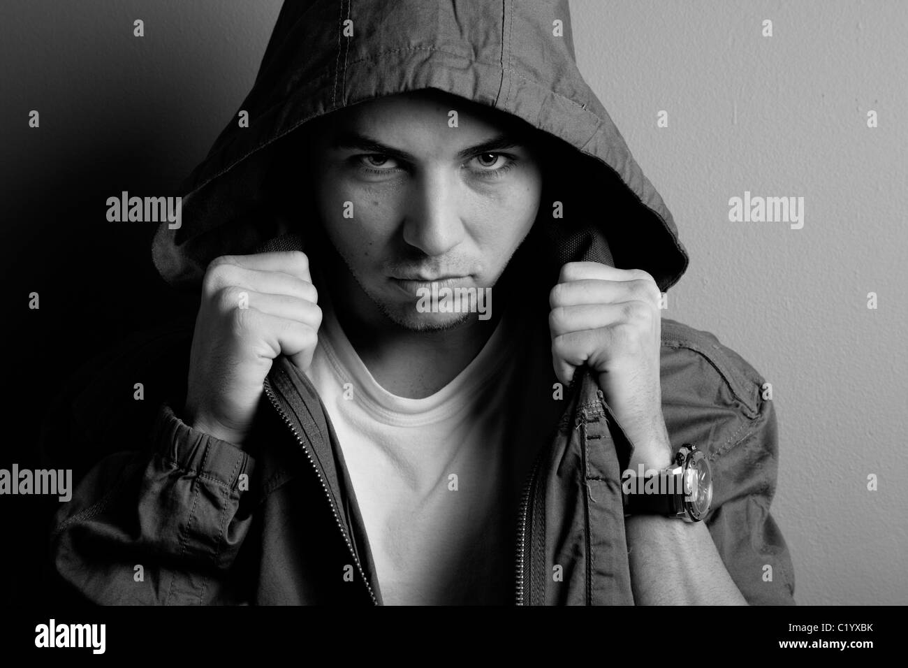 Photo of young adult male wearing hood, threatening expression on face. Stock Photo