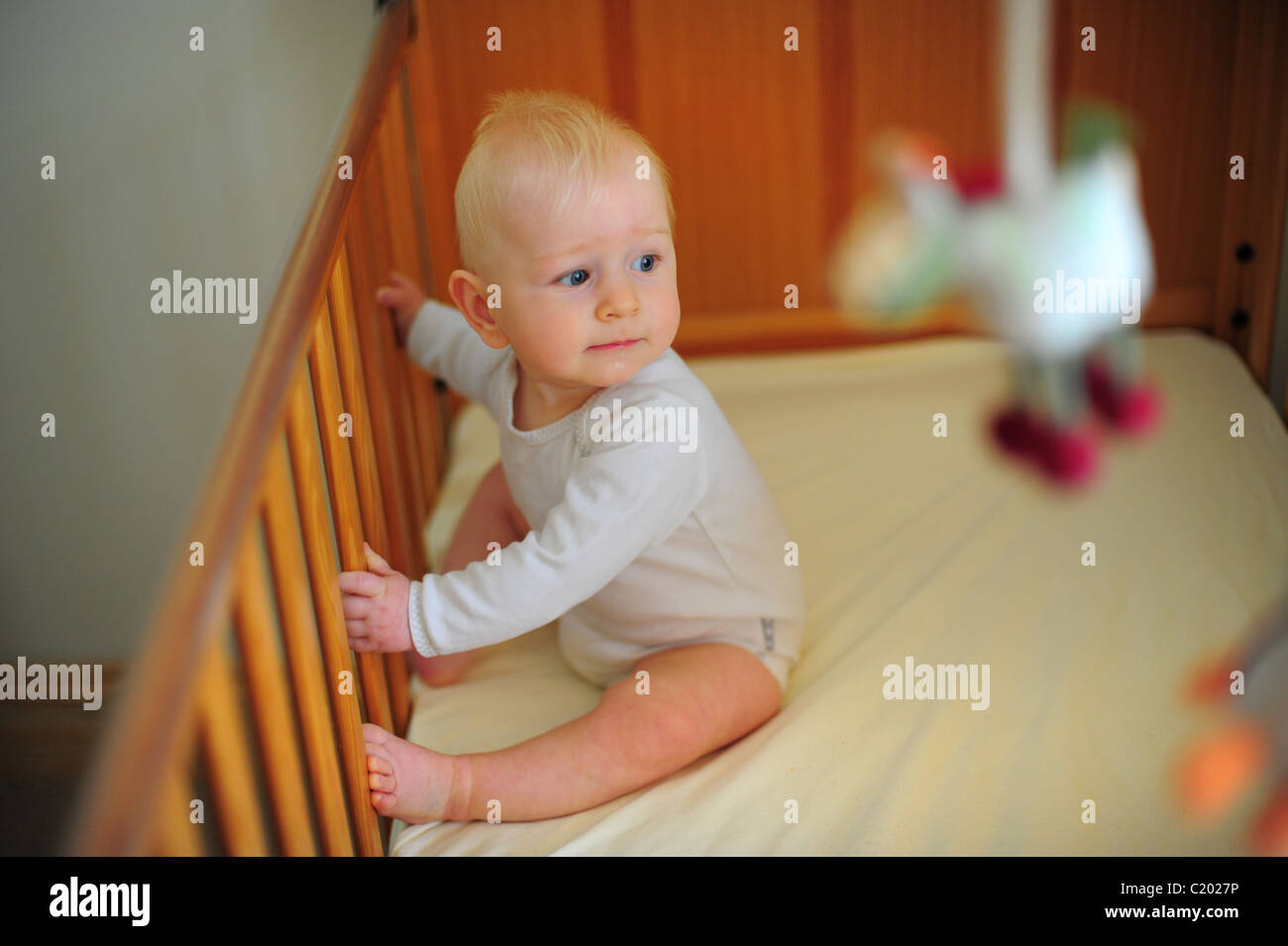 A one year old baby boy sitting in his cot in a bedroom or nursery