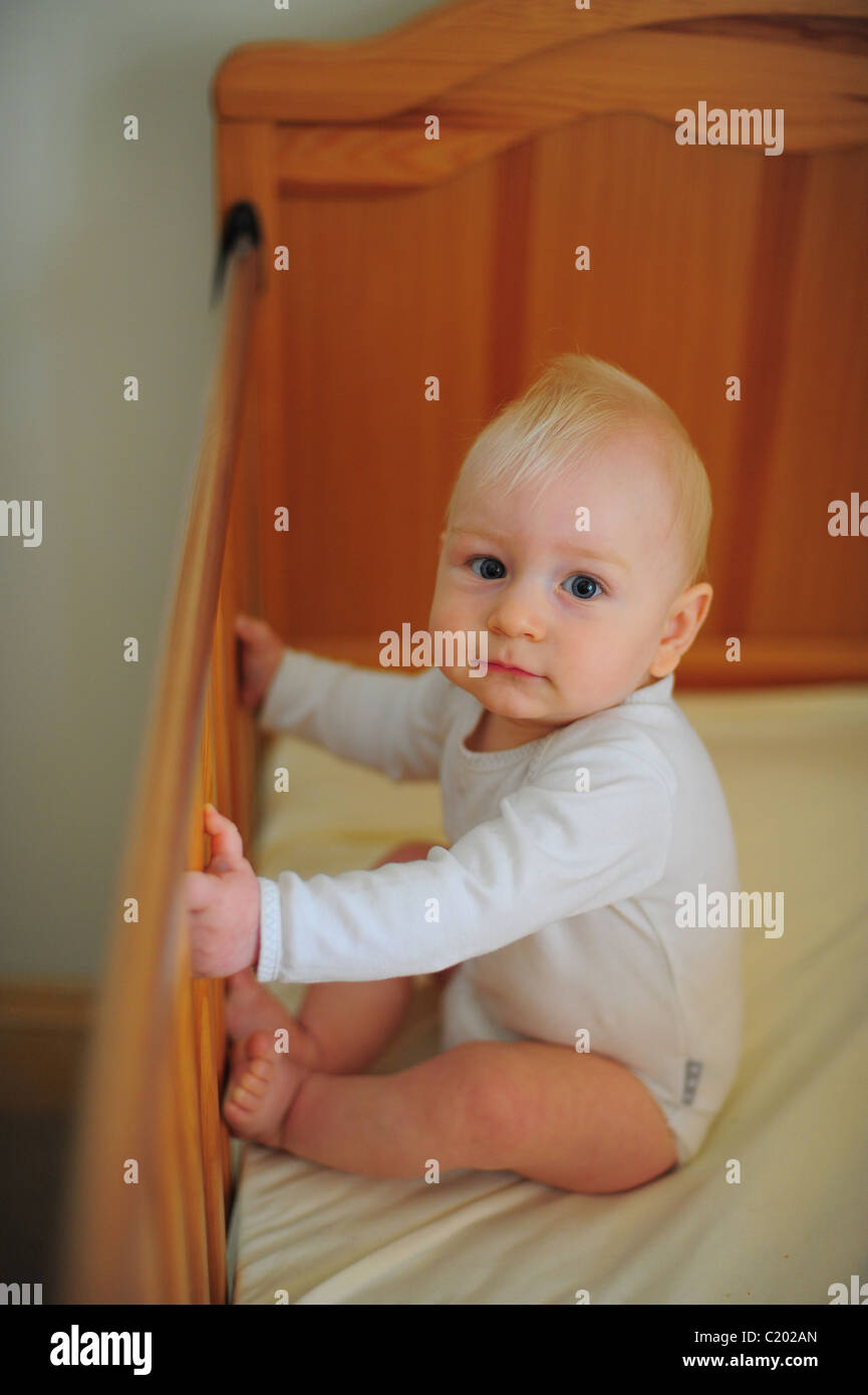 A One Year Old Baby Boy Sitting In His Cot At Home In A
