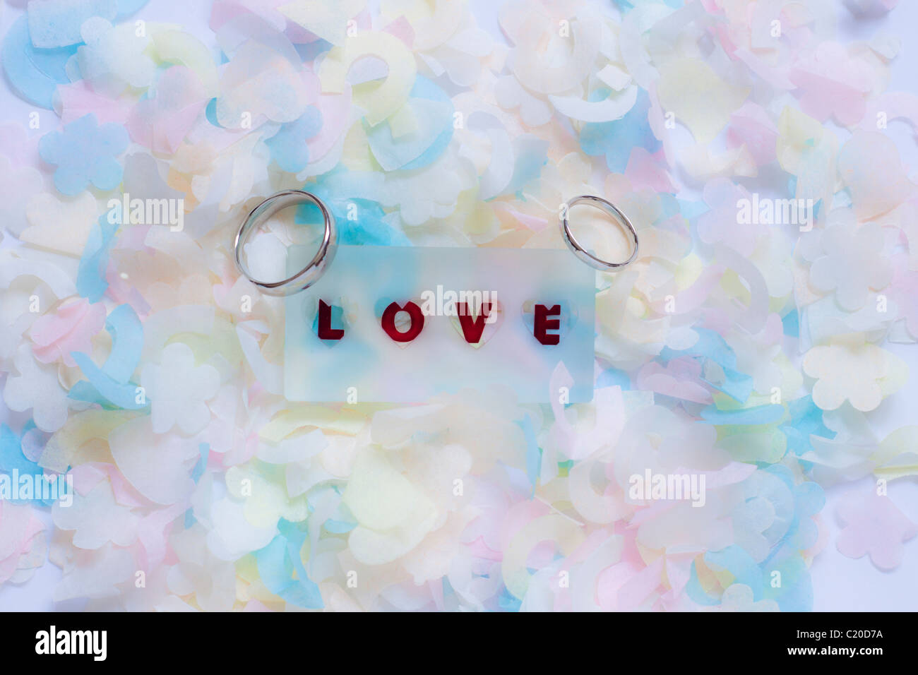 wedding rings either side of love token on a bed of confetti.copy space.landscape format Stock Photo