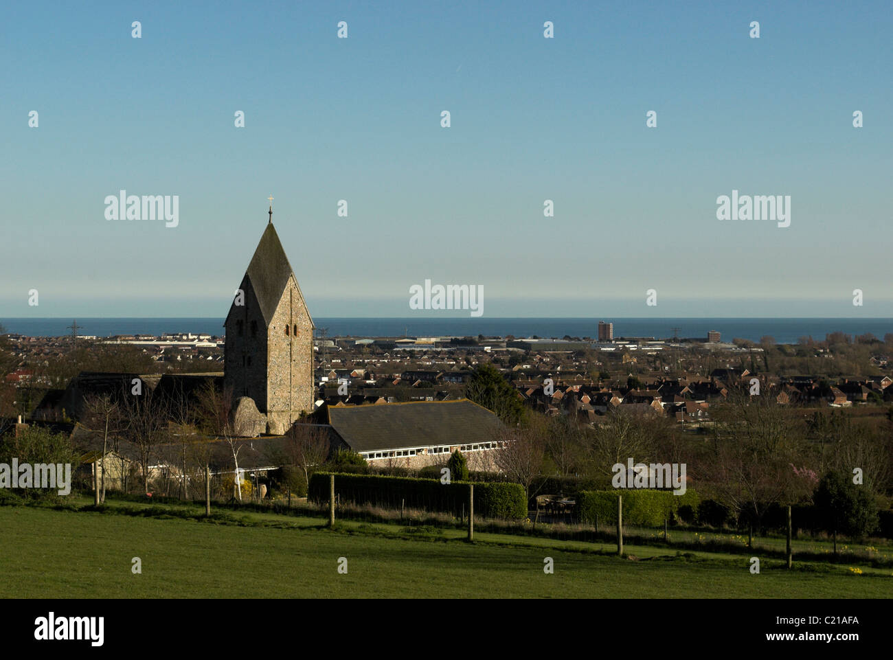 The Anglo-Saxon church of St Mary, Sompting, Sussex, nestling on the Downs with Sompting & Lancing and the sea in the background Stock Photo