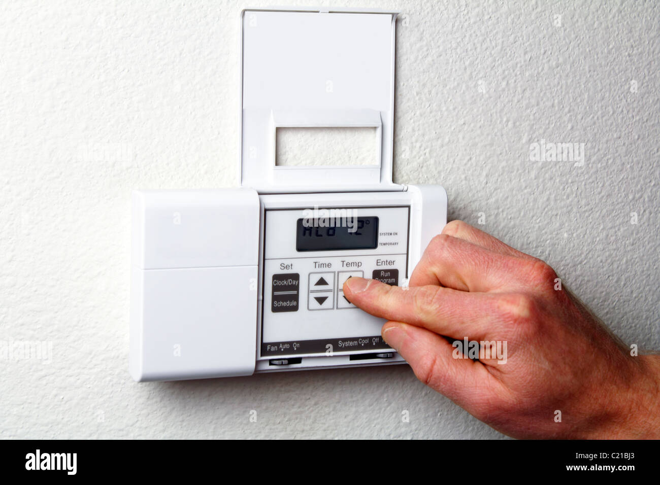 HVAC thermostat of a home heating energy system that is energy efficient. Fingers pushing controls on heating and cooling digital wall panel display. Stock Photo