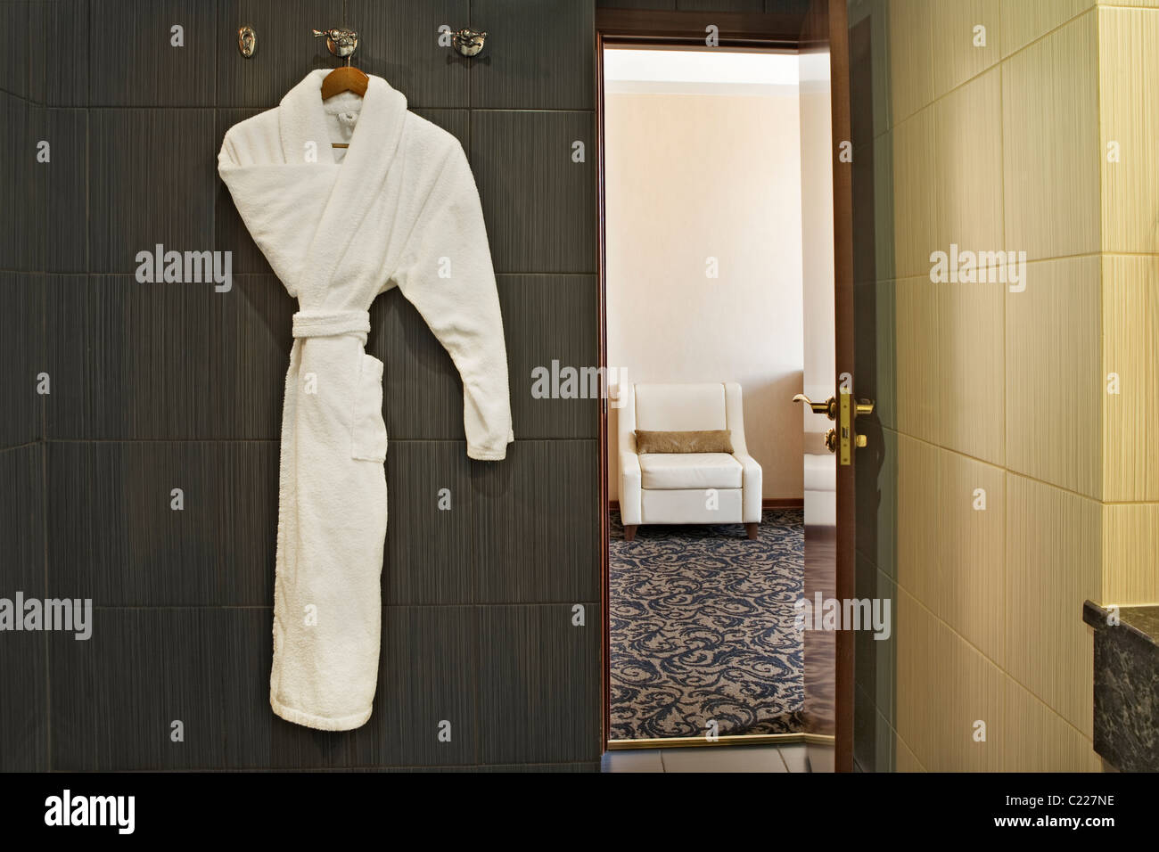 Interior of a hotel room with a white dressing gown hanging up and the door open with a view through to the next room Stock Photo