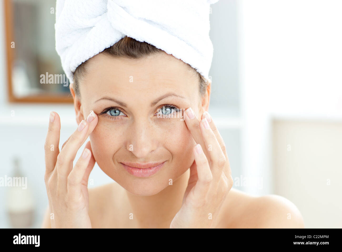 Cute young woman with a towel putting cream on her face in the bathroom