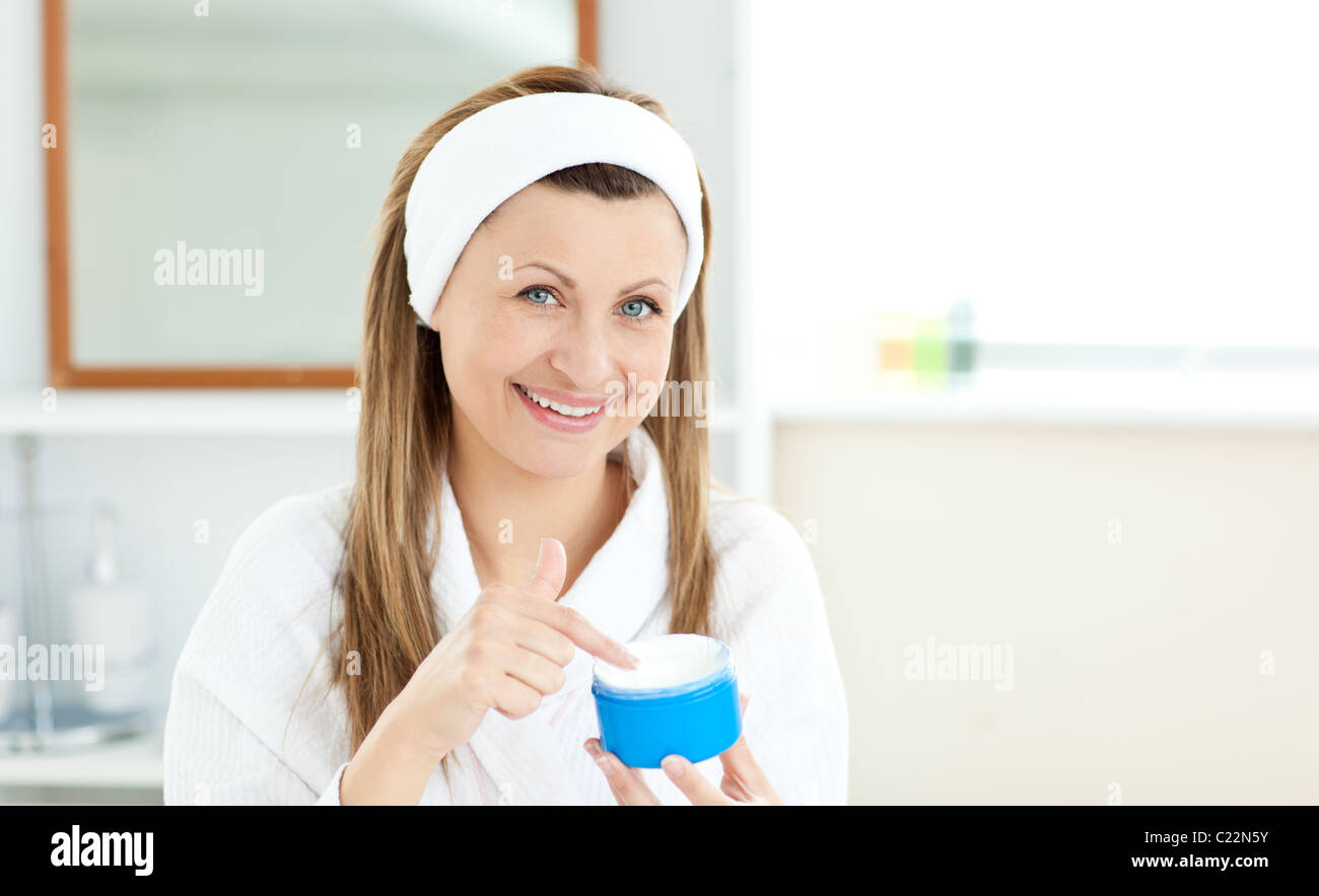 Delighted young woman putting cream on her face in the bathroom Stock