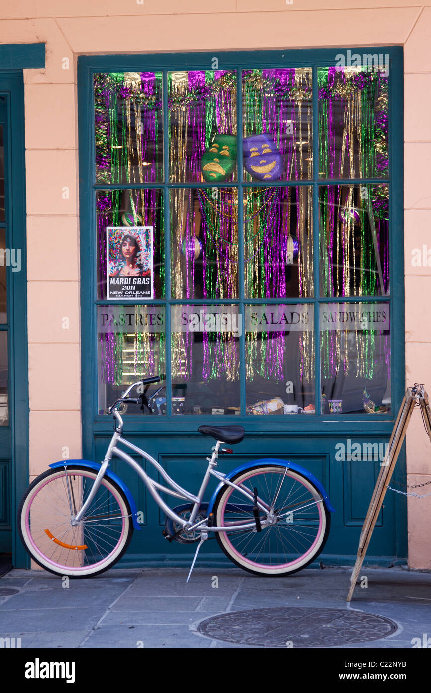 Bicycle parked on sidewalk in front of a cafe window decorated for Mardi Gras in the French Quarter of New Orleans Stock Photo