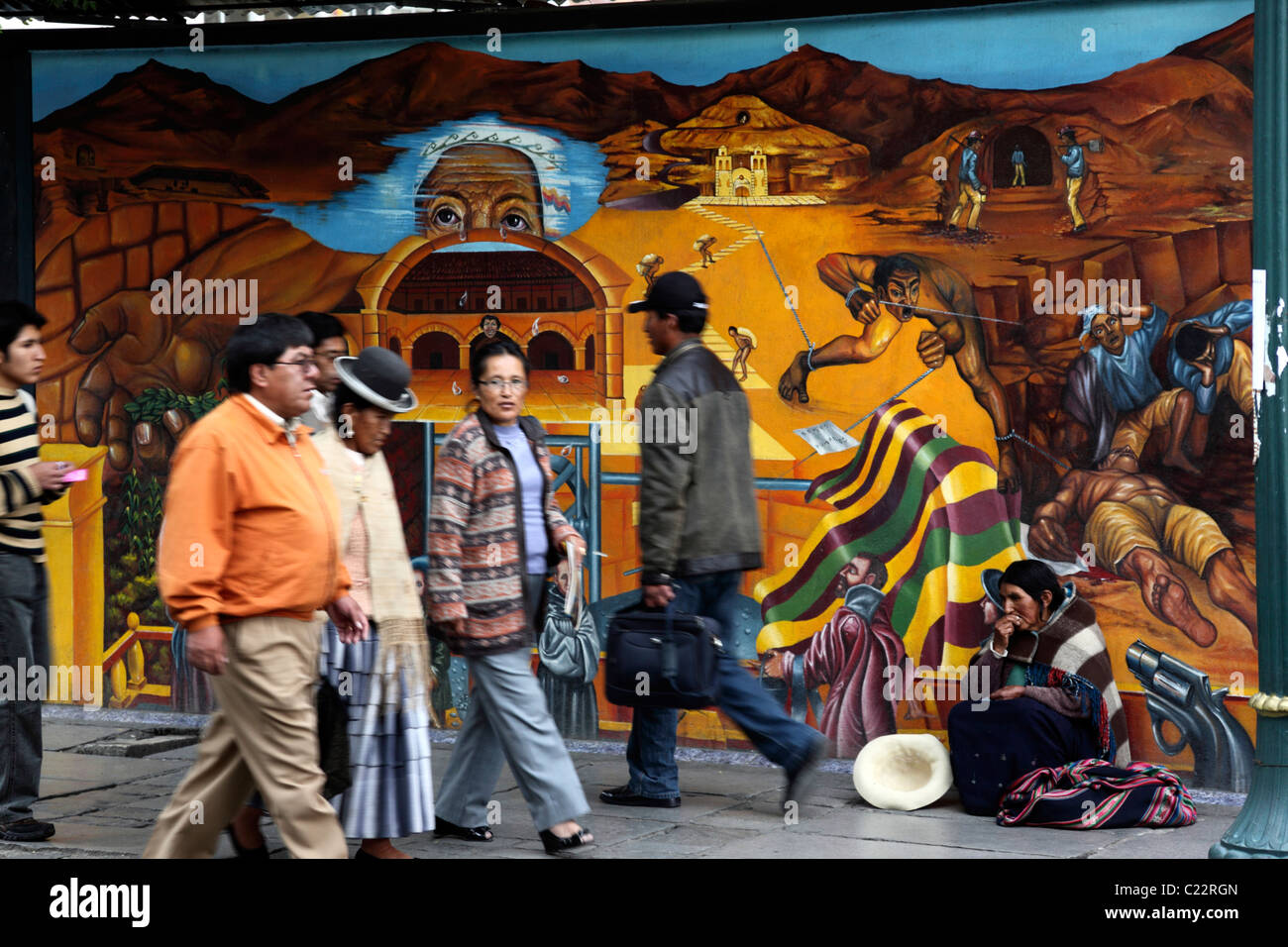 People walking past lady from Potosi region begging in front of mural showing repression of natives in Potosi silver mines in past, La Paz, Bolivia Stock Photo