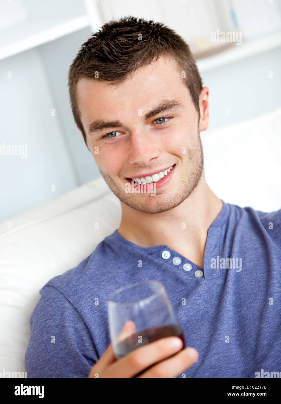 Handsome young man holding a glass of wine sitting on a sofa in the ...