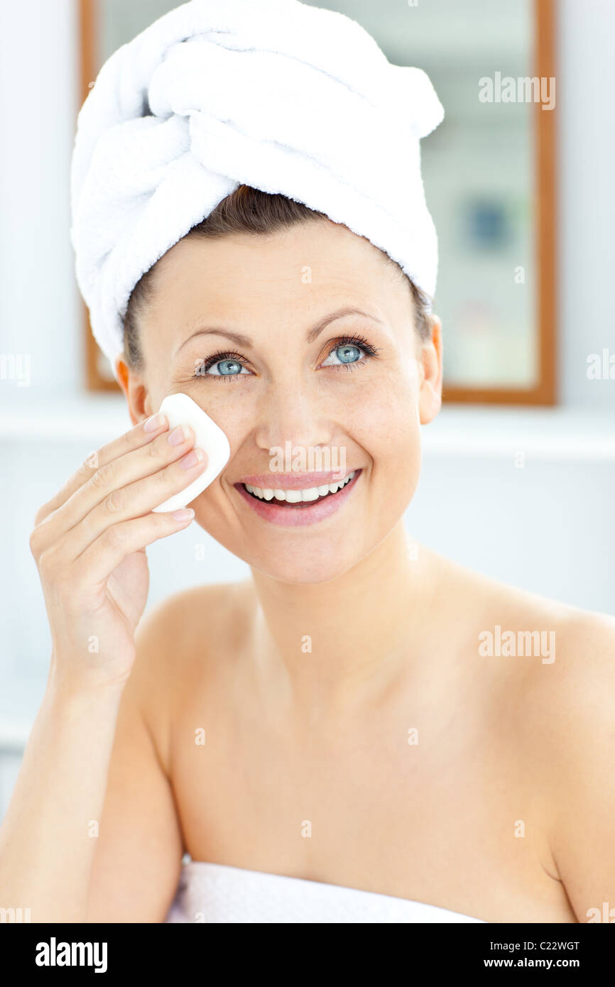 Smiling young woman with a towel putting cream on her face in the