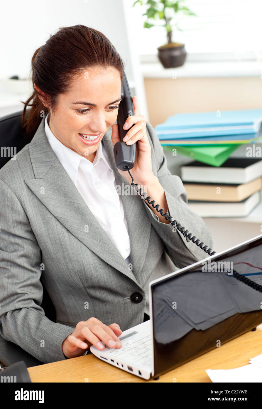 Busy businesswoman talking on phone and using her laptop sitting at her ...