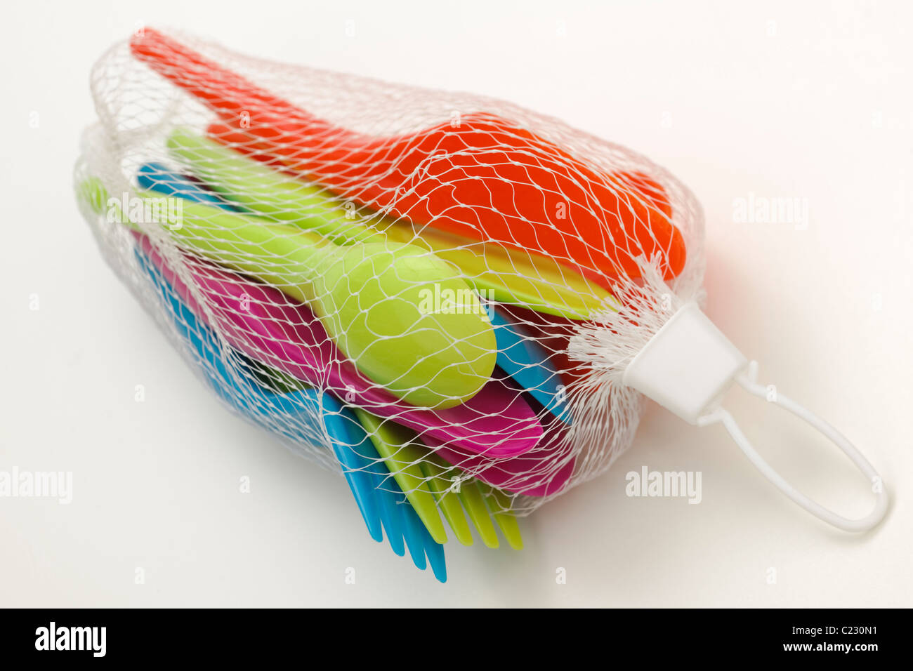 Set of brightly coloured plastic picnic knives forks and spoons in a white mesh bag Stock Photo